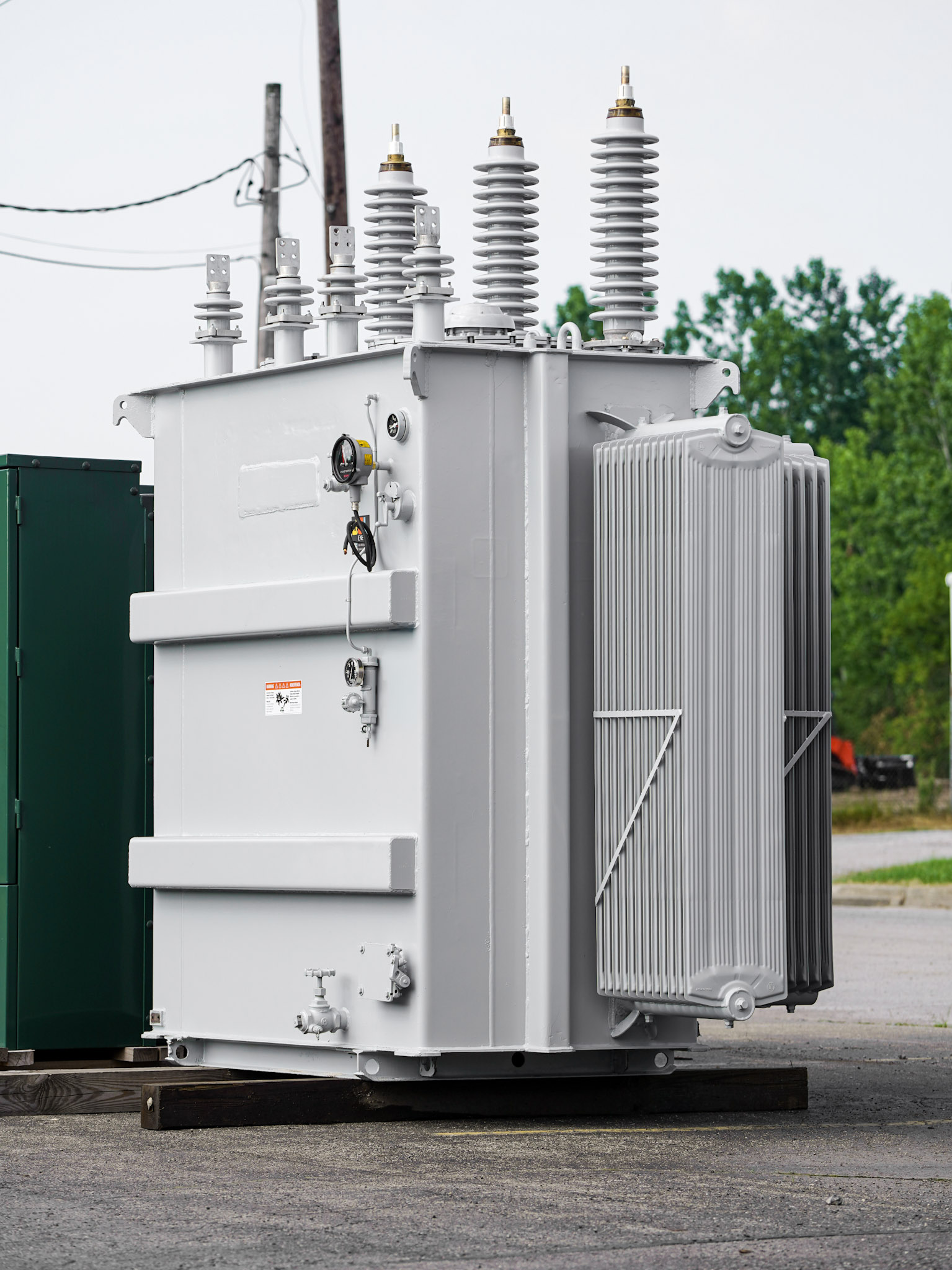 A gray substation transformer with HV bushings, arresters, radiators, and gauges