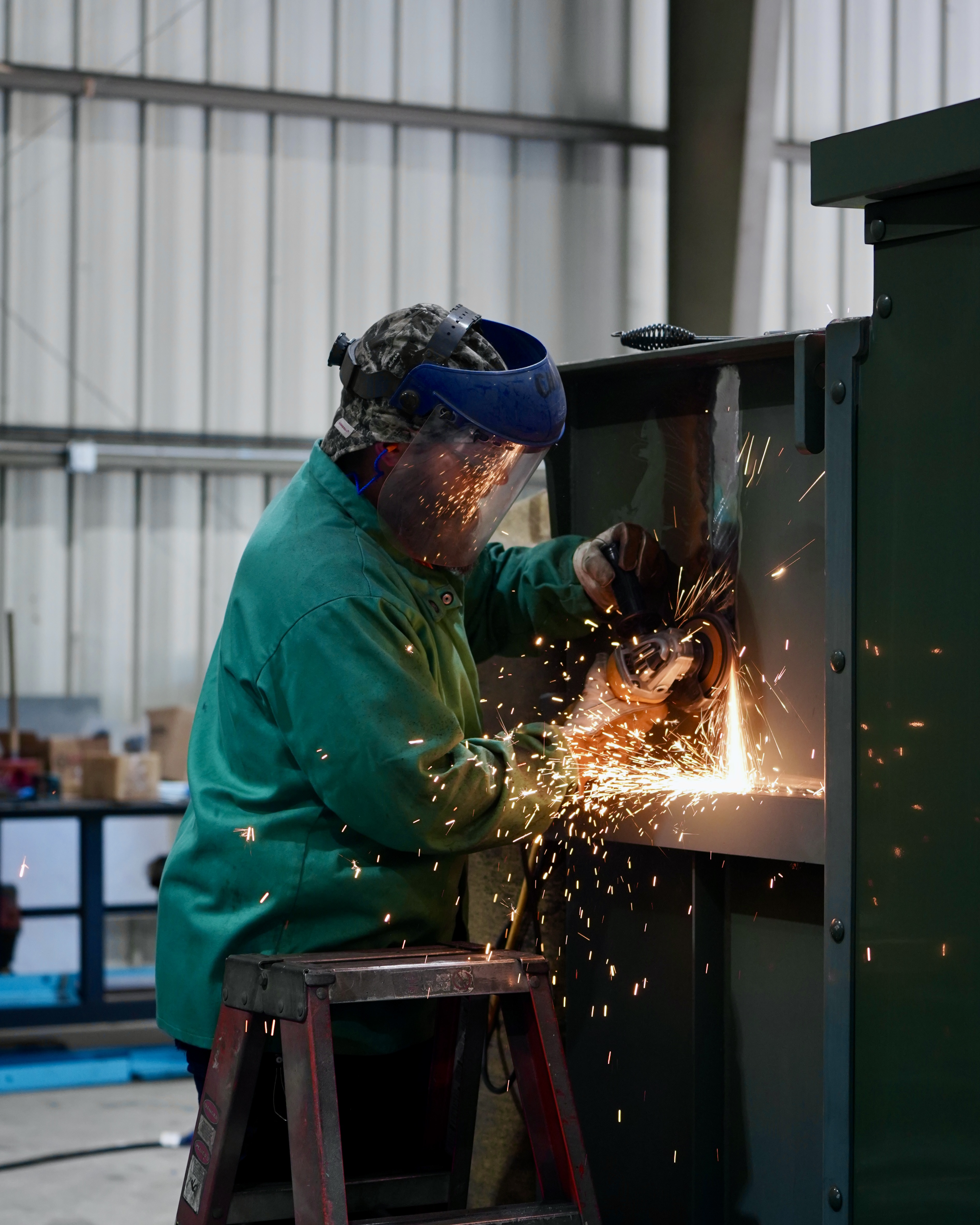 A JCL technician grinding a transformer cabinet in the shop, sparks flying
