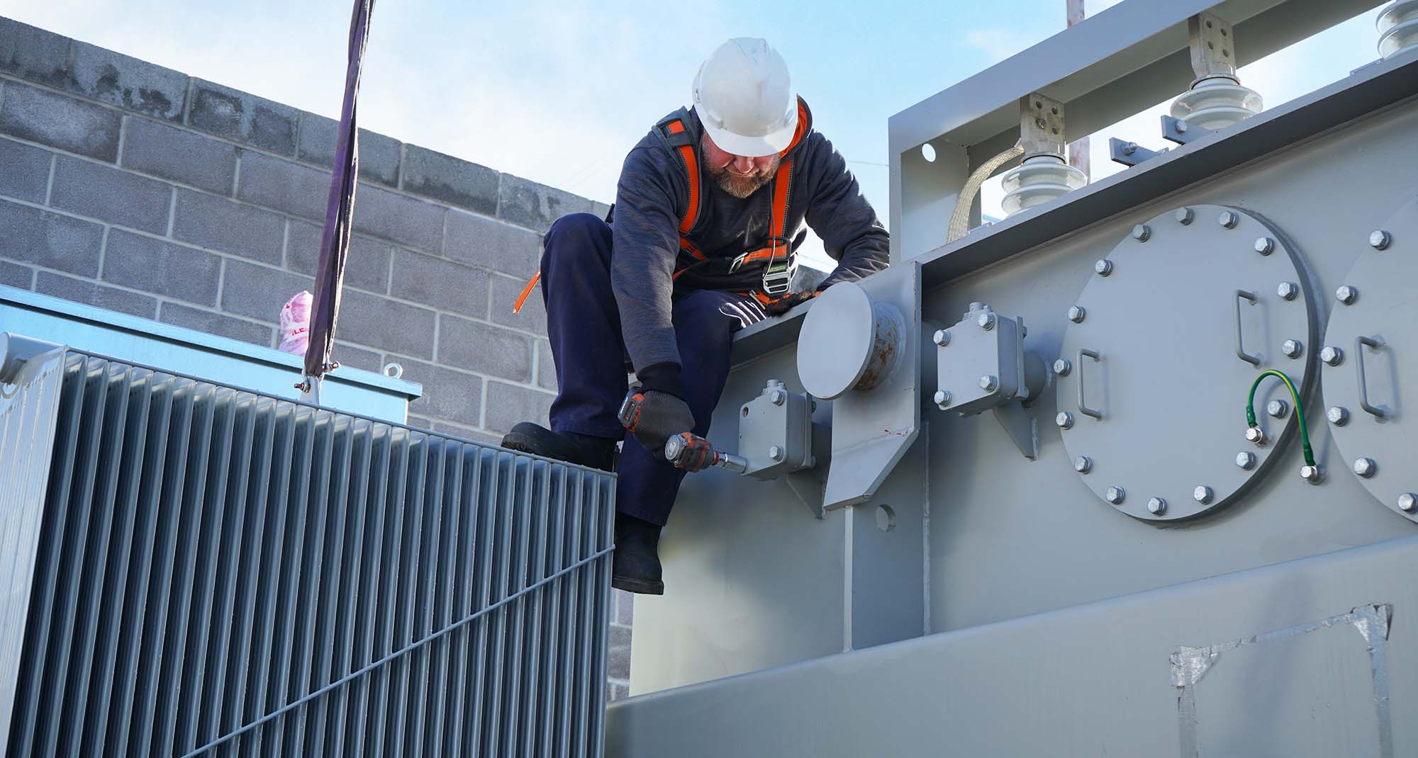 A JCL technician torquing hardware on top of a transformer tank